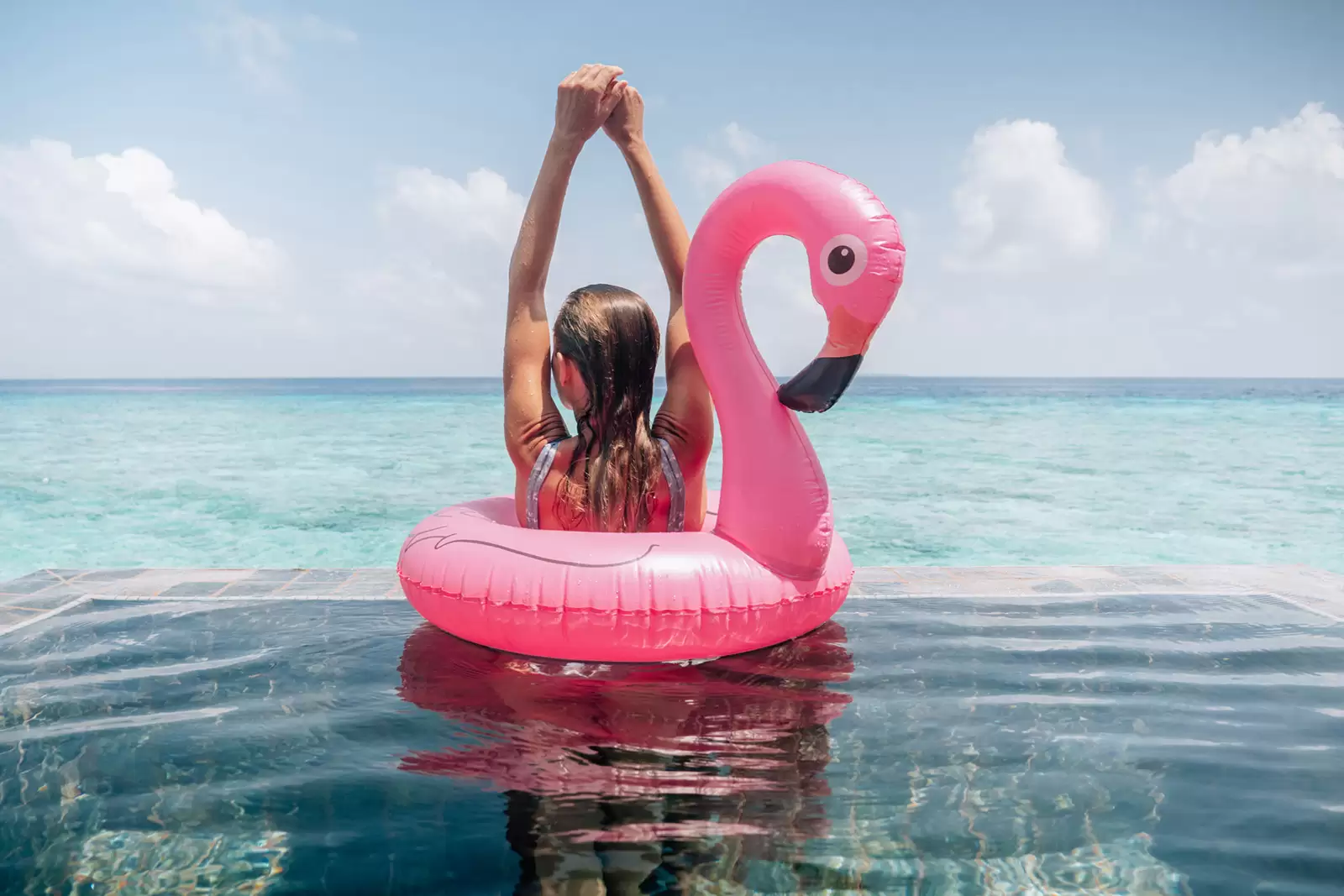 person-in-einem-pool-mit-aufblasbaren-flamingo-hebt-hände-in-die-luft