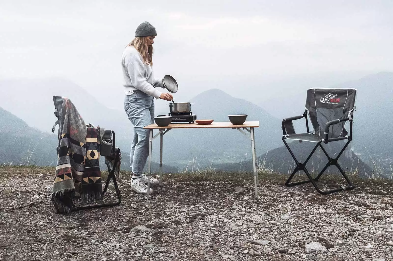 frau-kocht-mit-campingkocher-an-campingsitzgruppe